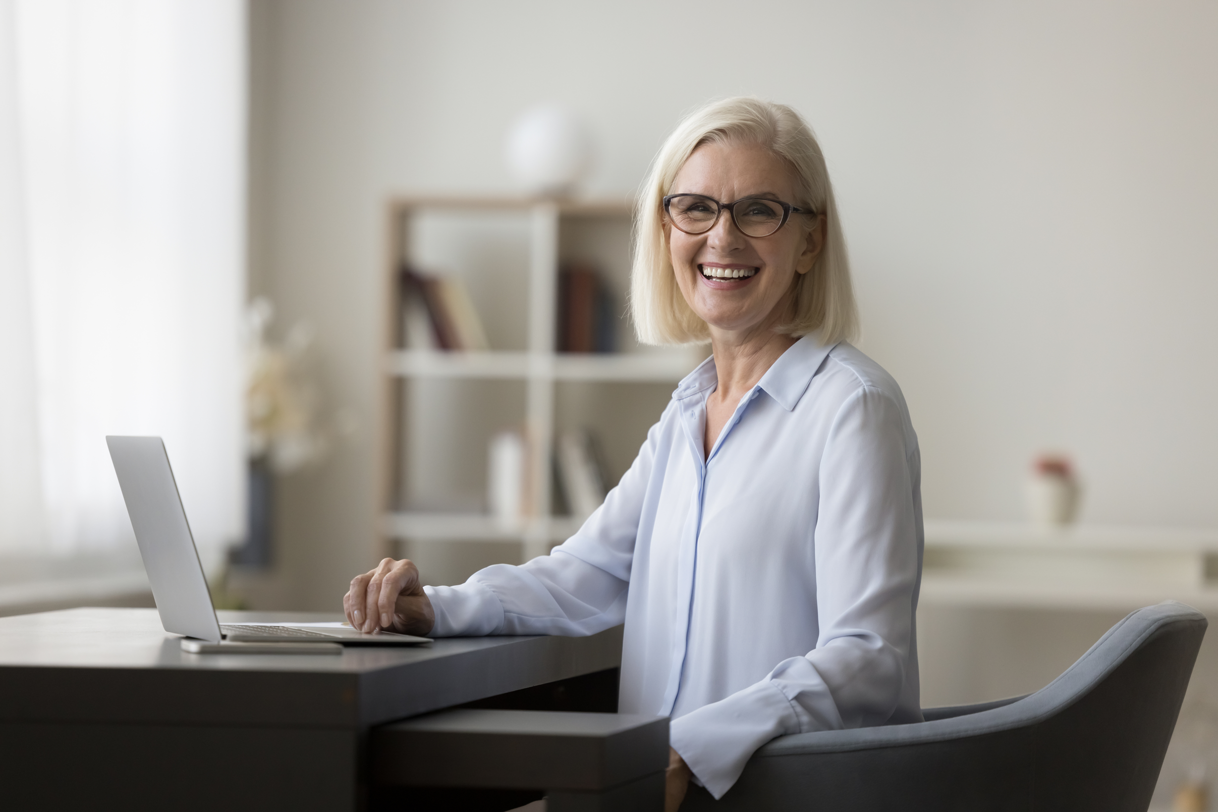 Businesswoman posing for camera seated at workplace desk with laptop Businesswoman posing for camera seated at workplace desk with laptop