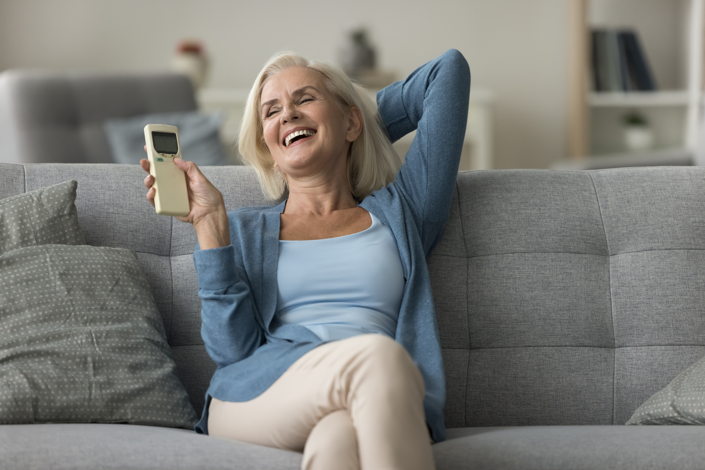 Woman switch-on air conditioner relaxing on sofa in living room Woman switch-on air conditioner relaxing on sofa in living room
